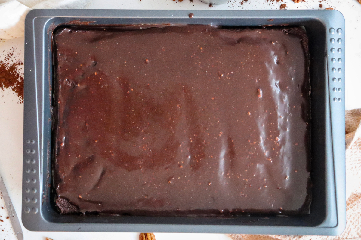 Frosting over chocolate cake before adding chopped nuts. 