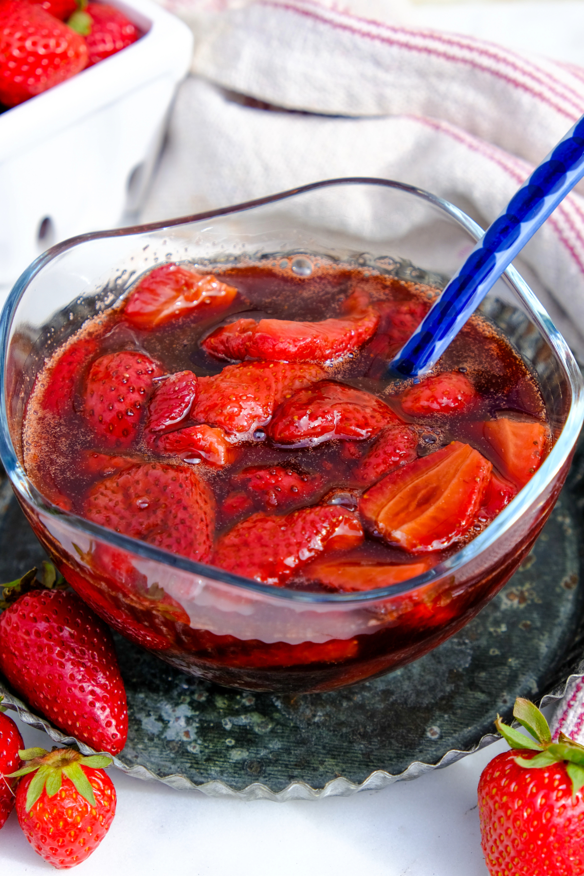 A clear glass bowl of roasted basalmic strawberries with a blue spoon.