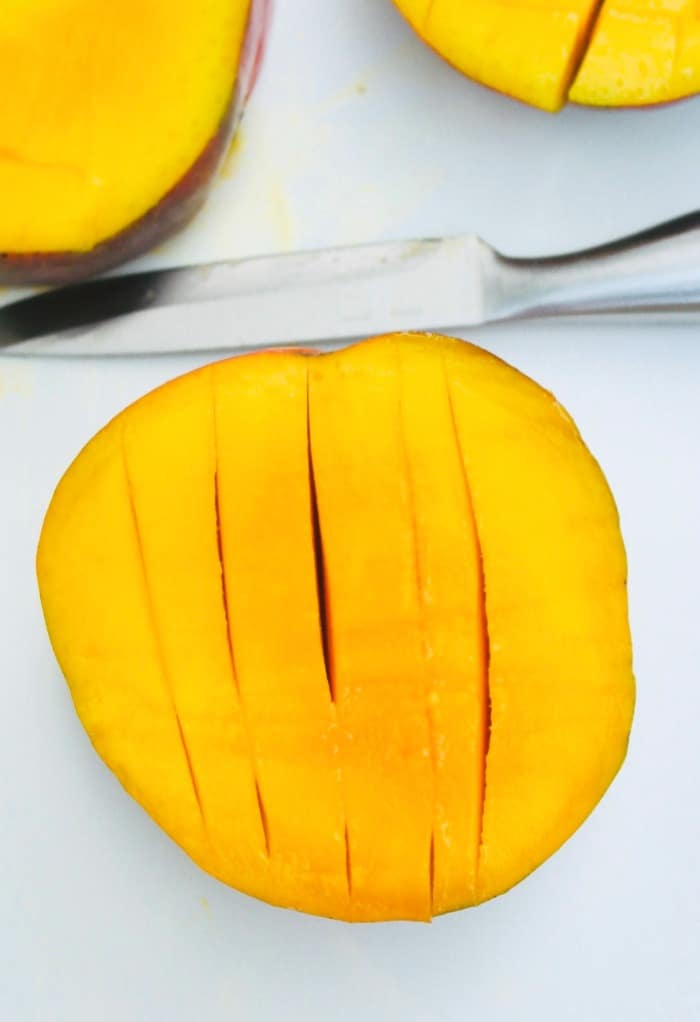 A half of a mango with vertical slices cut into the manto.