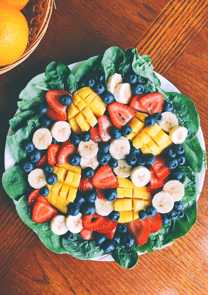 Large fruit salad over greens on a white plate. 