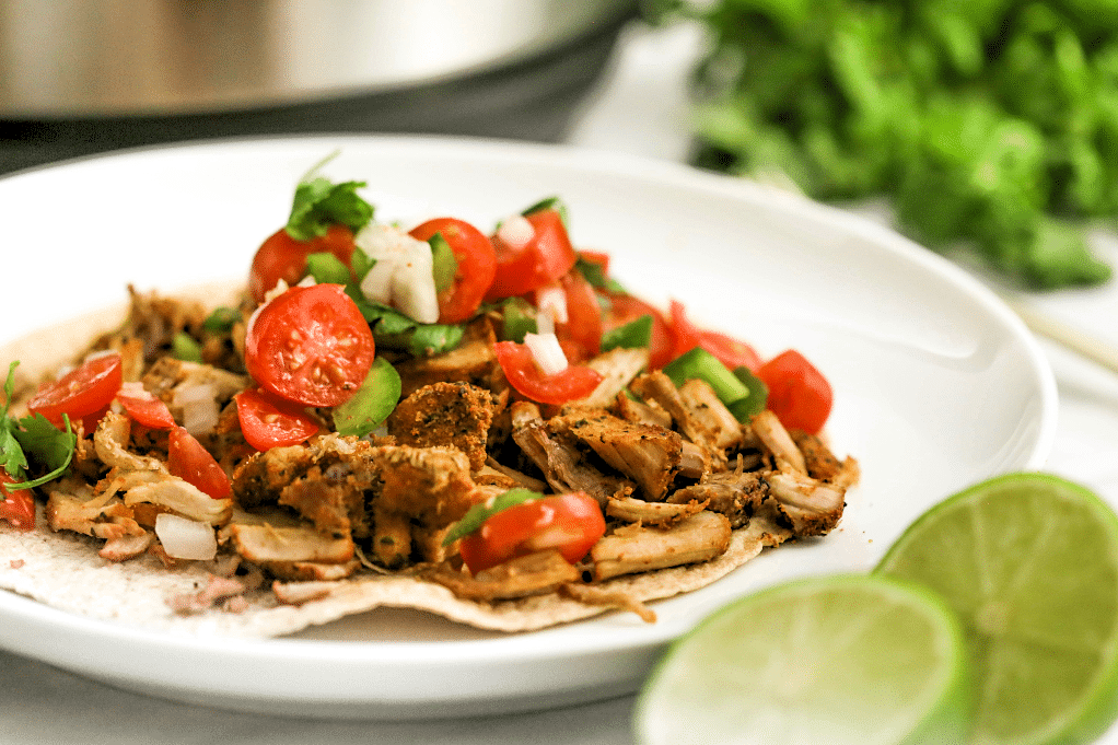 Pork carnitas on a white plate with fresh lime on the side. 