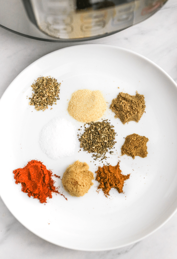 Spices on a white plate to be mixed together for carnitas. 