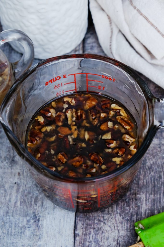 Homemade maple syrup with pecans in a large glass measuring cup.