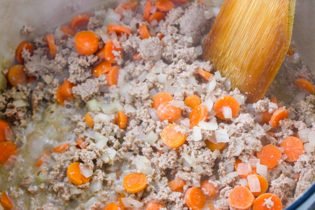 Cooked ground turkey with diced onion and carrots in a Dutch oven.