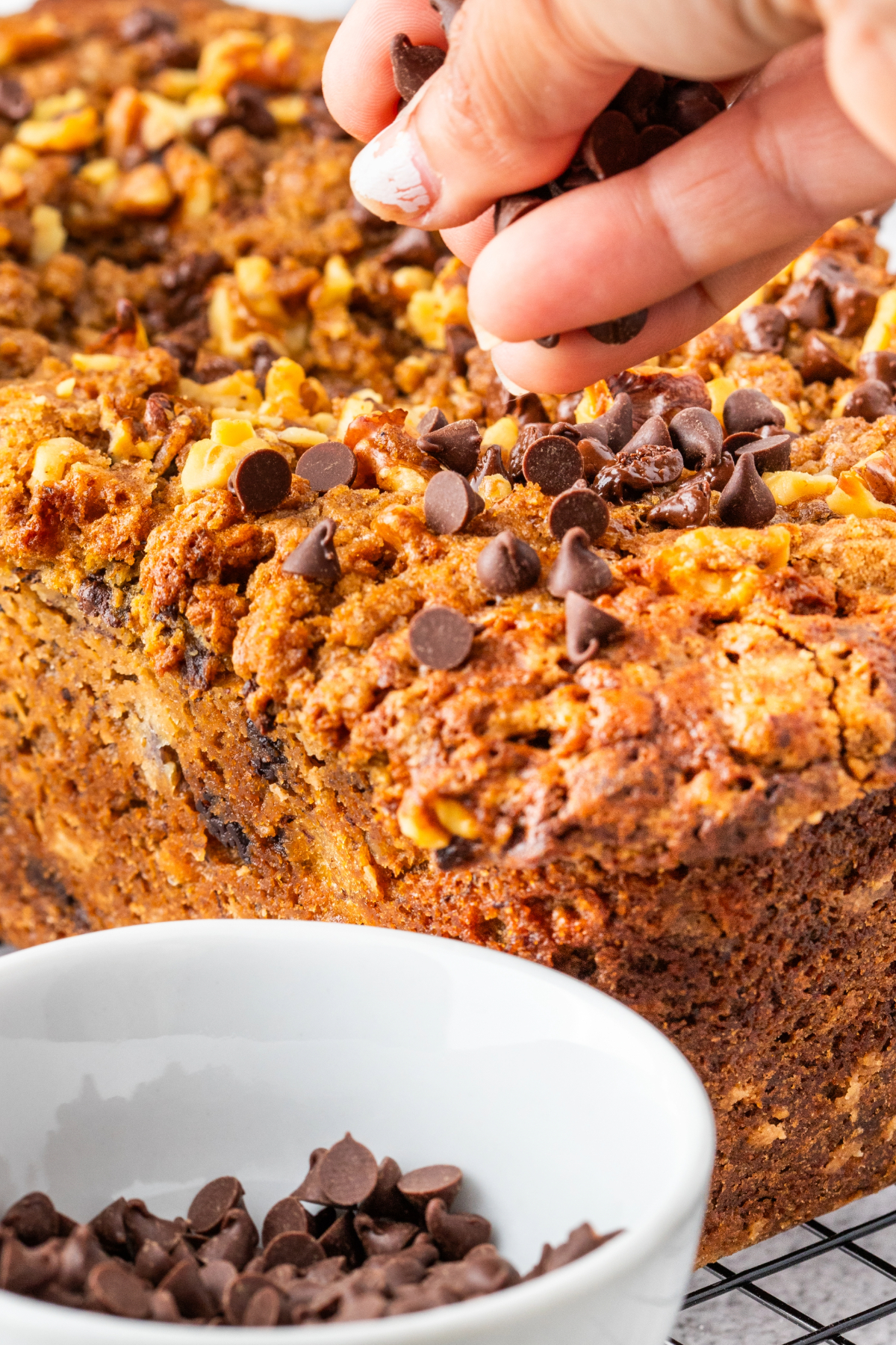 Adding chocolate chips to the top of baked banana bread on a cooling rack. 