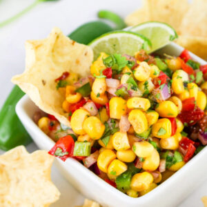 Chipotle corn salsa in a small white dish with a tortilla chip dipping into the salsa.