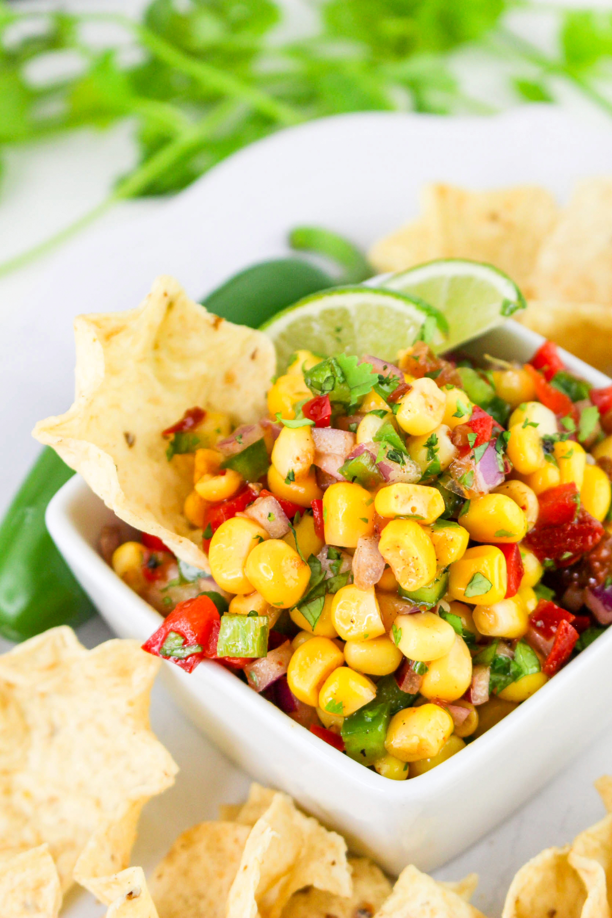 Fresh corn salsa in a white square bowl surrounded with scoop tortilla chips.