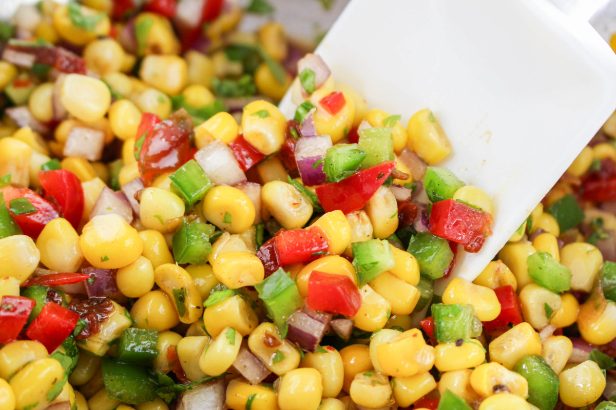 All corn salsa ingredients mixed together with a white rubber spatula. 