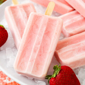 Strawberry banana protein popsicles on a white tray over ice cubes.