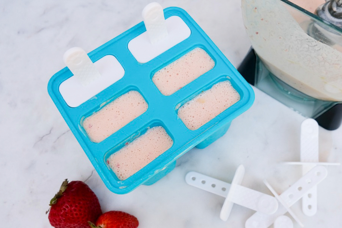 Homemade popsicle fruit mix with strawberries and yogurt poured into molds before freezing. 