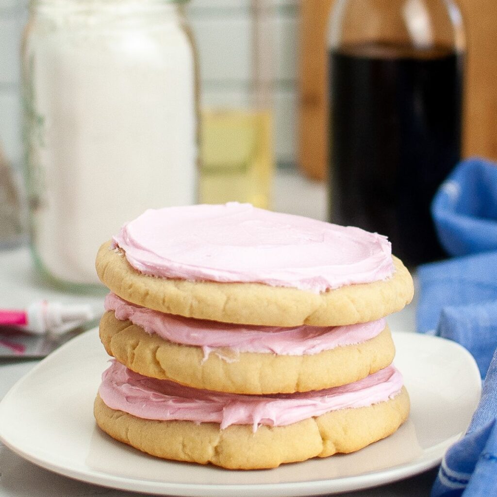 Three copycat Crumbl Pink Sugar Cookies stacked on top of each other on a small plate.