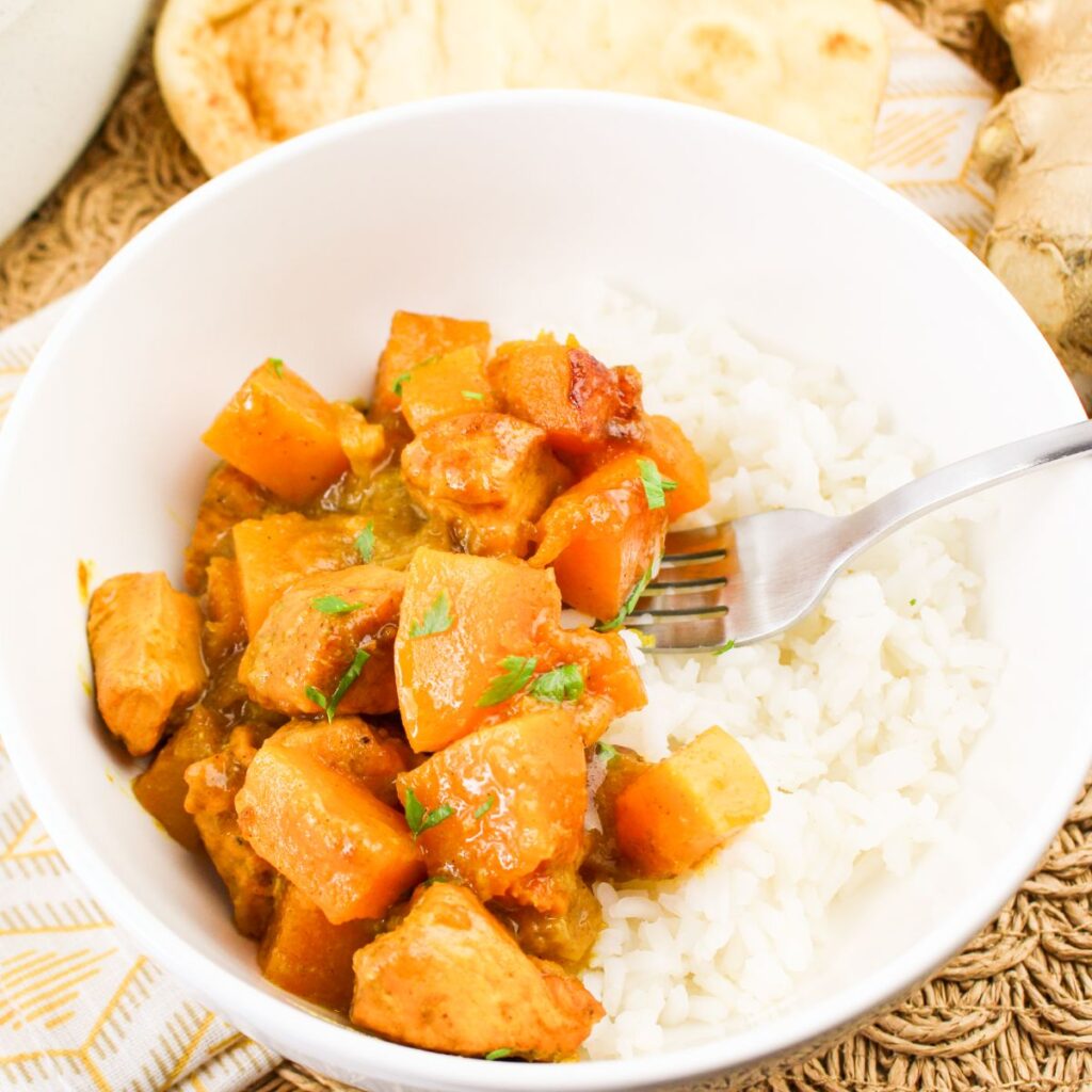 Serving of pumpkin chicken curry in a bowl served over a bed of white rice.