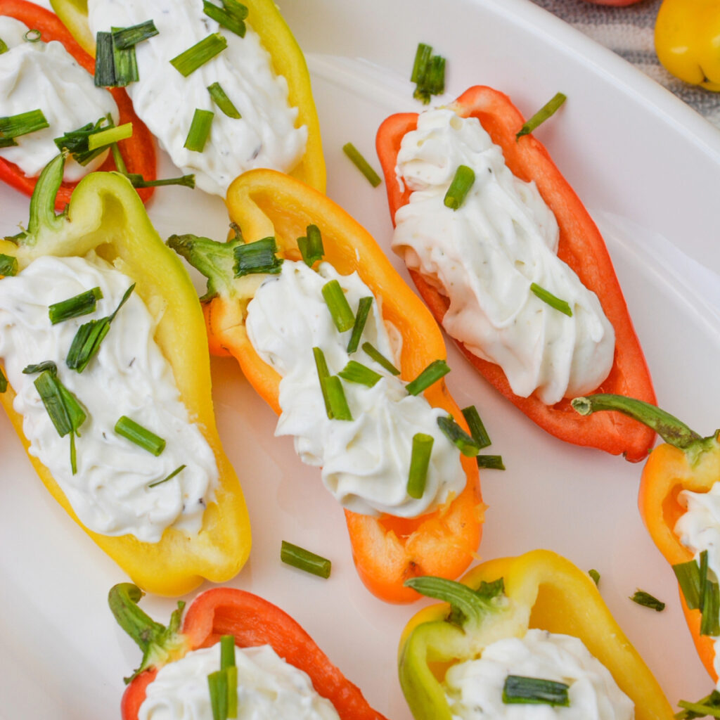 Goat cheese stuffed peppers on a white platter, topped with chopped chives.